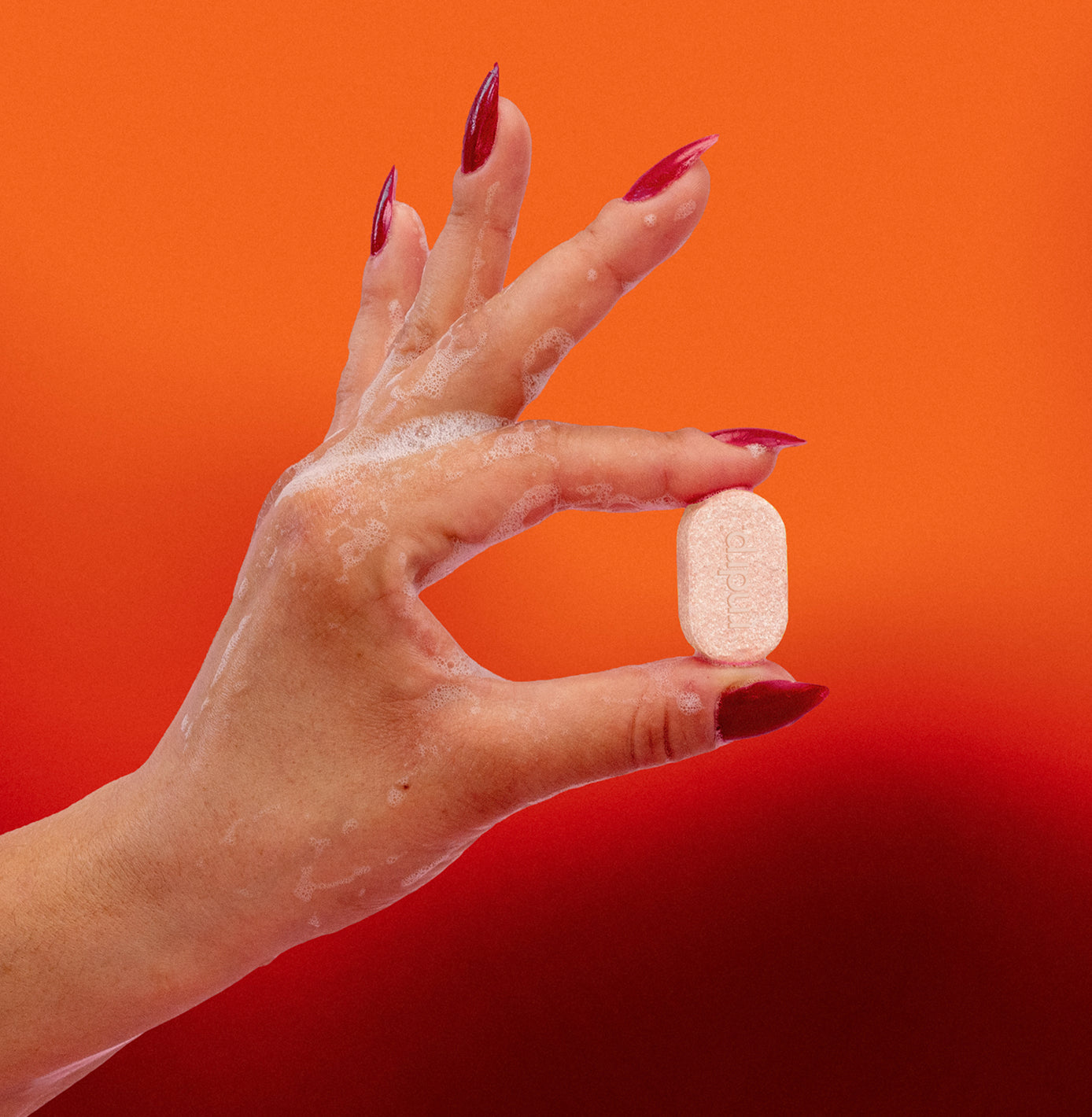 Hand holding an orange rndrp hand soap tablet against an orange background