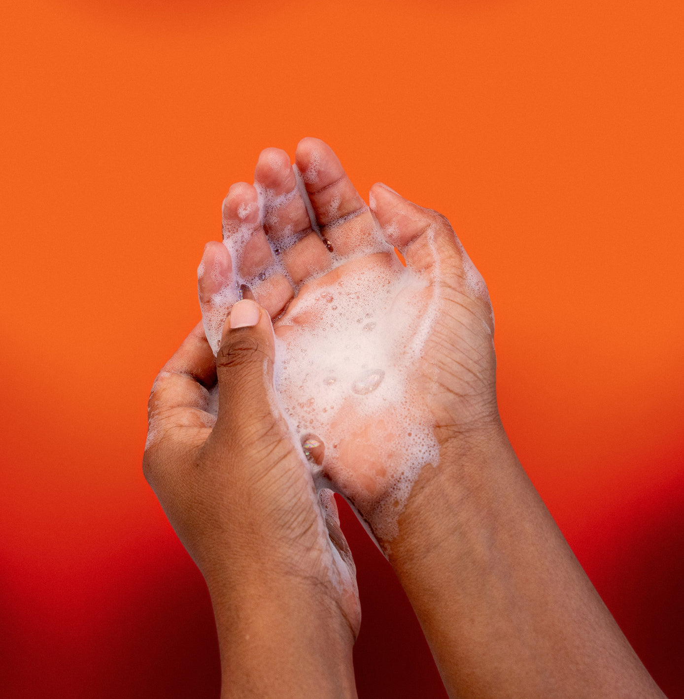 Hands with soap suds against an orange background