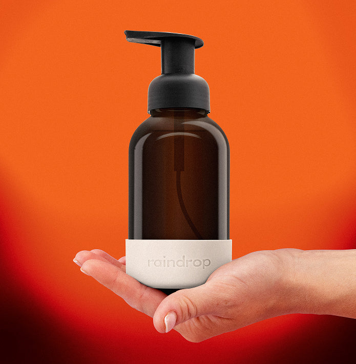 Brown soap dispenser with black pump held in a hand against an orange background